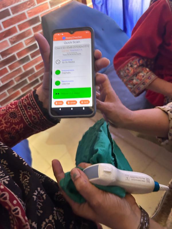 A health worker holds a phone showing a pregnancy scan result beside a handheld ultrasound probe