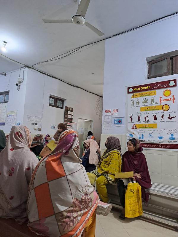 Women waiting in a hospital outpatient area beside a heat-stroke awareness poster