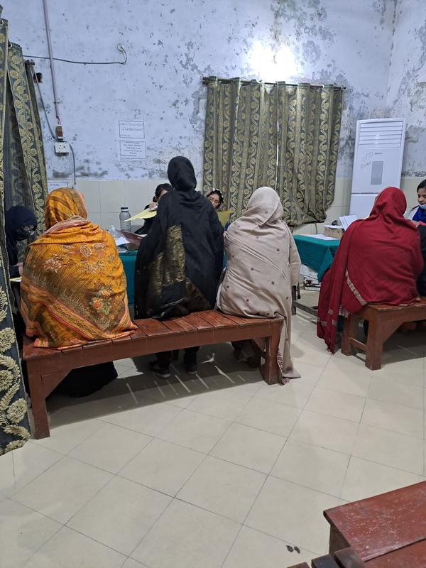 Patients on a wooden bench in a clinic, facing staff at a desk